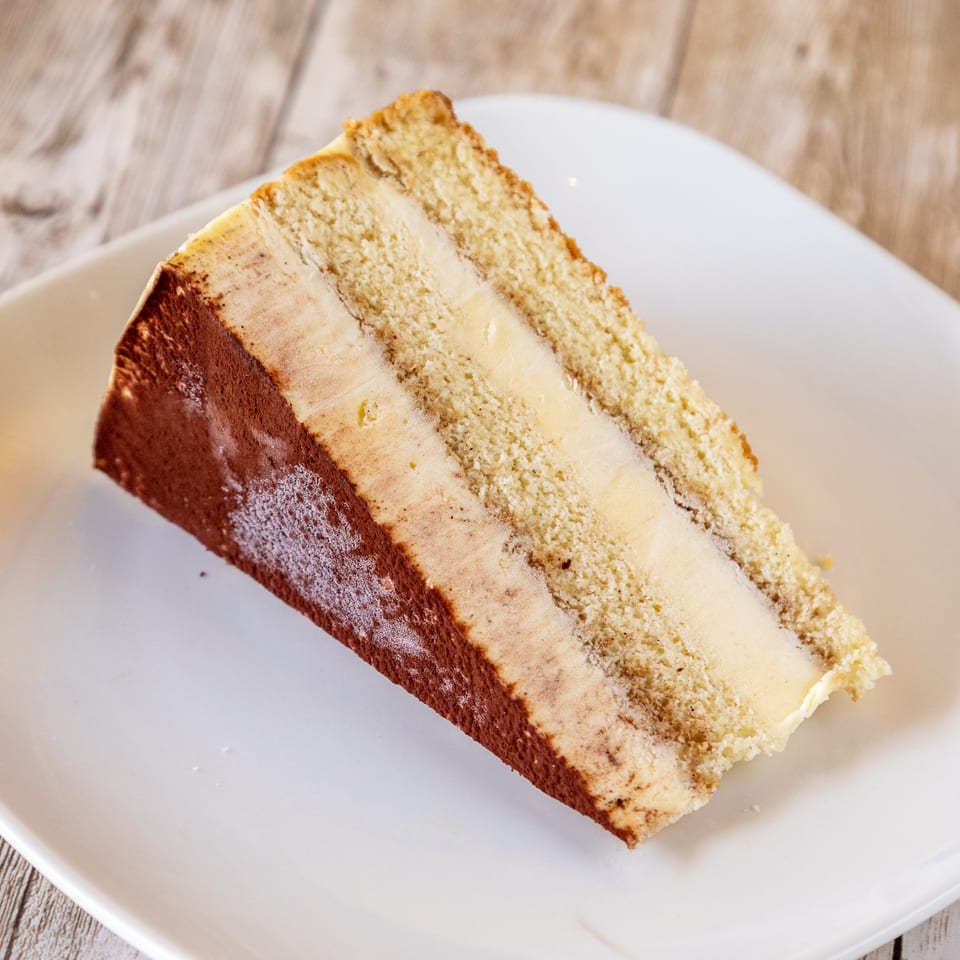 A slice of tiramisu cake with layers of sponge cake and cream, dusted with cocoa powder.