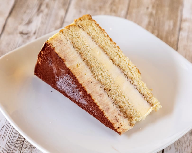 A slice of tiramisu cake with layers of sponge cake and cream, dusted with cocoa powder.