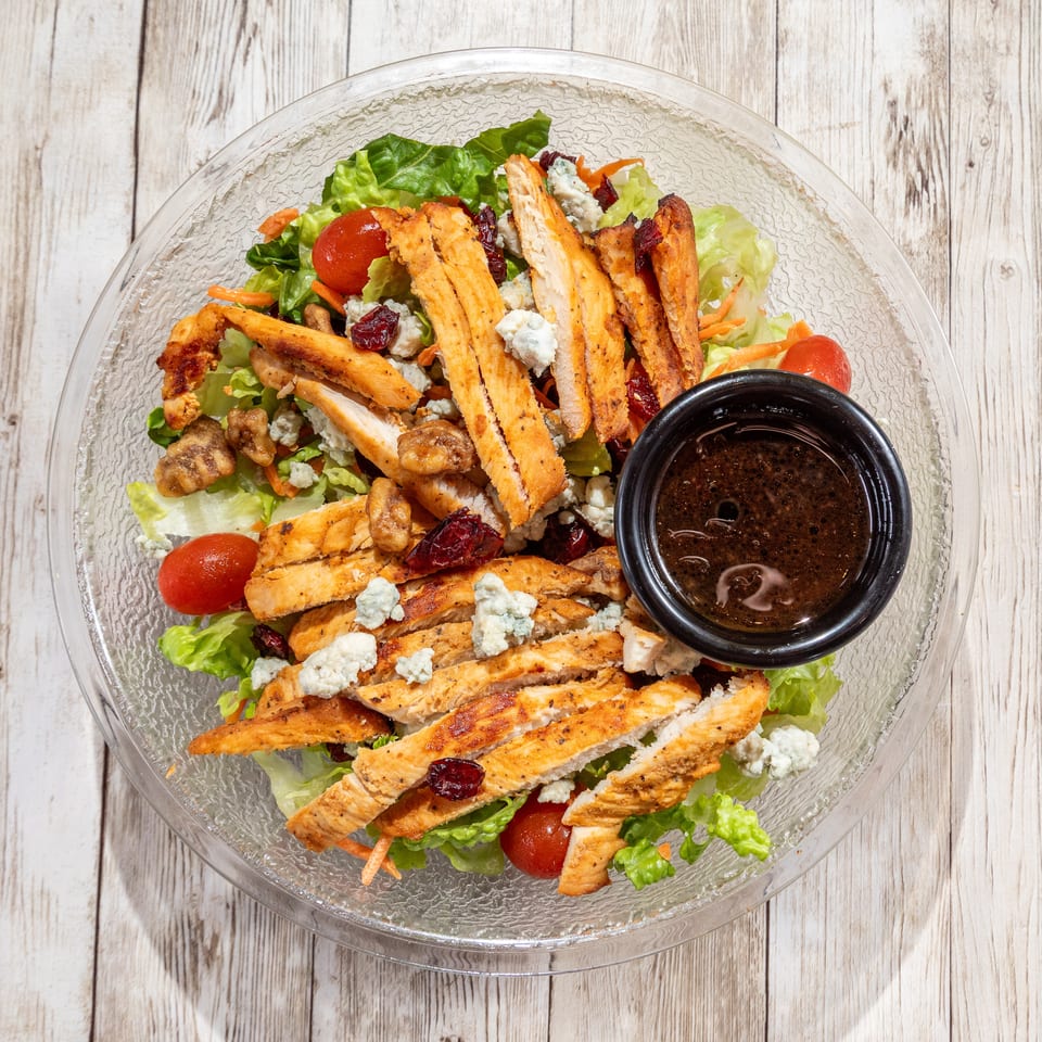 Overhead view of a chicken salad with blue cheese, cranberries, walnuts, and dressing.
