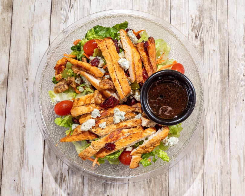 Overhead view of a chicken salad with blue cheese, cranberries, walnuts, and dressing.