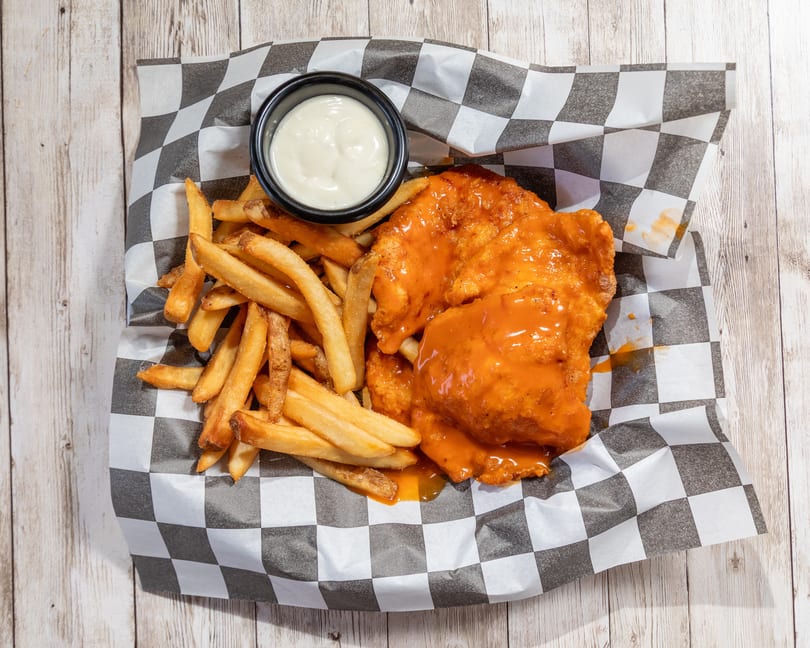 Buffalo chicken tenders and french fries with a side of ranch dressing on checkered paper.