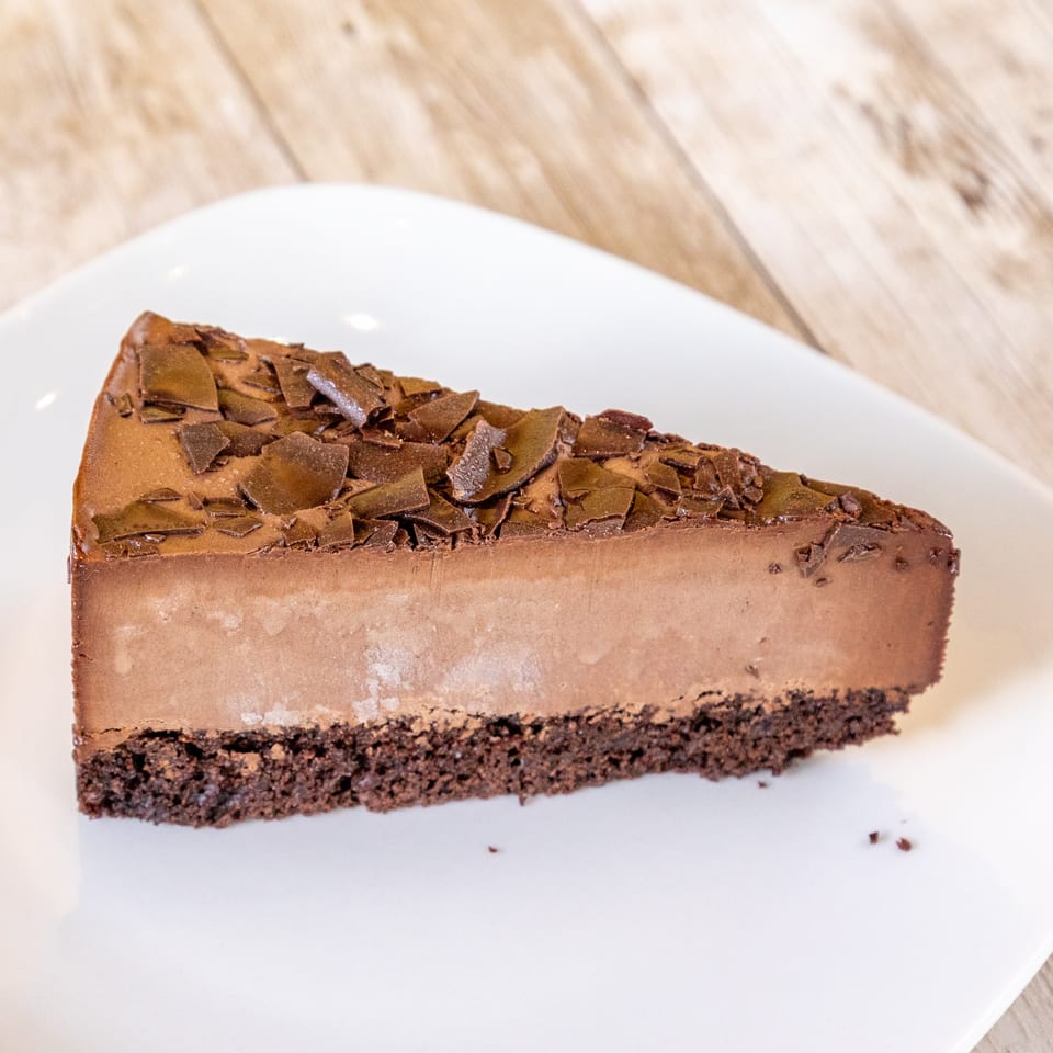 A slice of rich chocolate cheesecake with chocolate shavings on top, on a white plate.